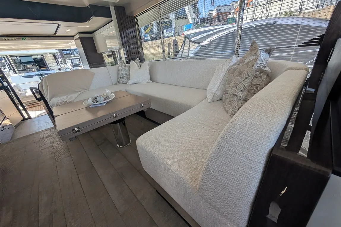Stylish indoor seating area with a beige sofa, decorative cushions, and a small table on wooden flooring, overlooking a marina.